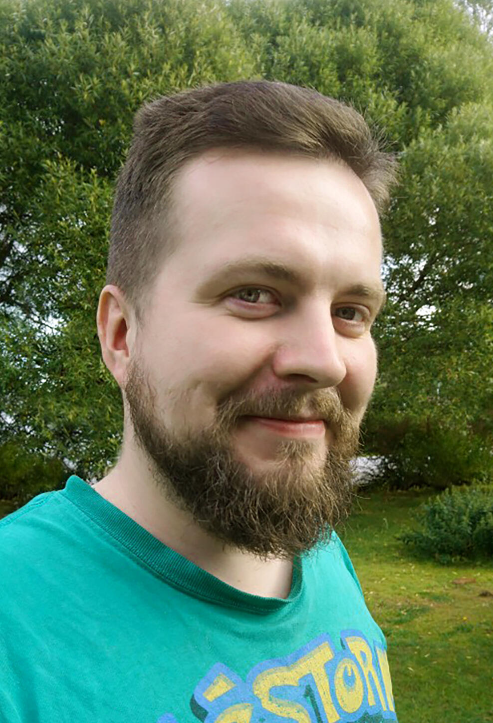 A photograph of Jakub Wisz, a smiling short-haired man with a beard and green Alestorm t-shirt